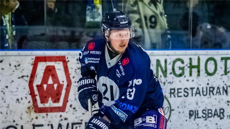 Eishockeyspieler in blauer und gelber Ausrüstung mit Schläger und Puck auf dem Eis, Zuschauer im Hintergrund.
