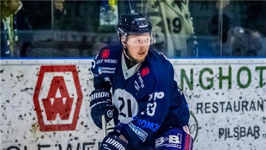 Eishockeyspieler in blauer und gelber Ausrüstung mit Schläger und Puck auf dem Eis, Zuschauer im Hintergrund.