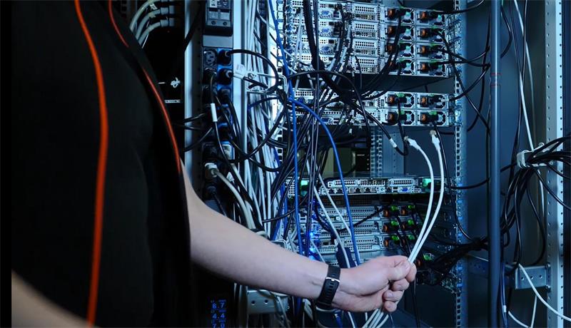 An einem Serverschrank sind etliche Kabel und Stecker zu sehen.