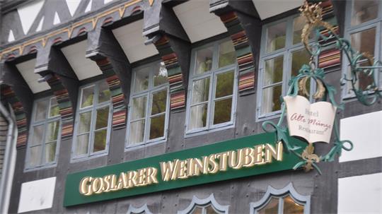 Fachwerkhausfassade mit mehreren Fenstern und einem grünen Schild mit goldener Aufschrift 'GOSLARER WEINSTUBEN'