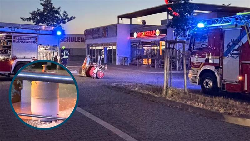 Feuerwehrautos mit Blaulicht vor einem Gebäude mit der Aufschrift 'Döner Kebab' und einem vergrößerten Ausschnitt einer Gasflasche am Straßenrand. 
