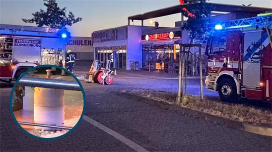 Feuerwehrautos mit Blaulicht vor einem Gebäude mit der Aufschrift 'Döner Kebab' und einem vergrößerten Ausschnitt einer Gasflasche am Straßenrand. 