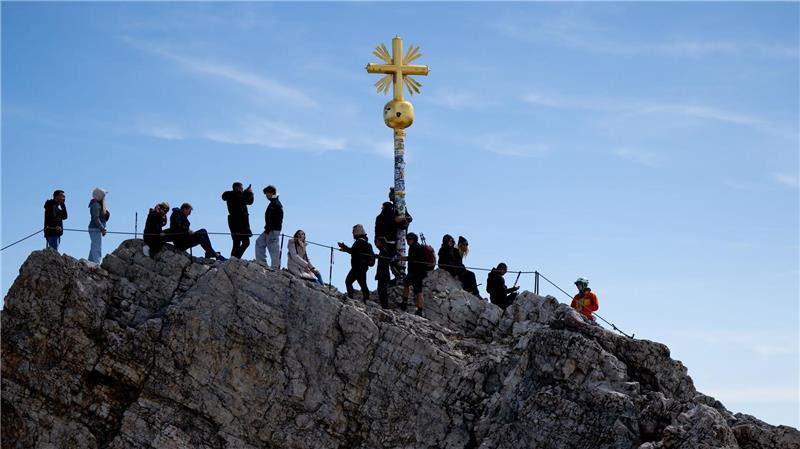 Ausflügler genießen das schöne Wetter am Gipfelkreuz auf der Zugspitze.