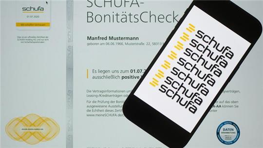 Smartphone mit mehrfach wiederholtem Schriftzug 'schufa' liegt auf einem SCHUFA-BonitätsCheck-Dokument mit persönlichem Namen und Geburtsdatum
