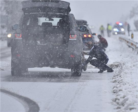 Autofahrer ziehen auf einer verschneiten Straße die Schneeketten auf. Foto: Verónica Lacasa, dpa
