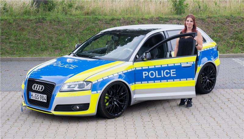 Autotunerin Svenja Geertz steht neben ihrem Audi, der ähnlich wie ein Polizeifahrzeug foliert ist und die Aufschrift „Police“ trägt.