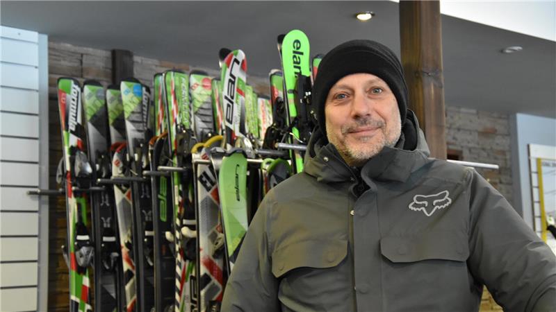 Person in grauer Jacke mit Fox-Logo steht vor einem Regal mit mehreren Skiern in einem Geschäft.