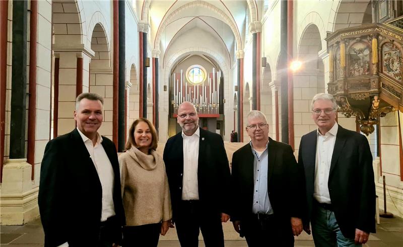 Vier Männer und eine Frau stehen im Kirchenschiff und lächeln in die Kamera. 