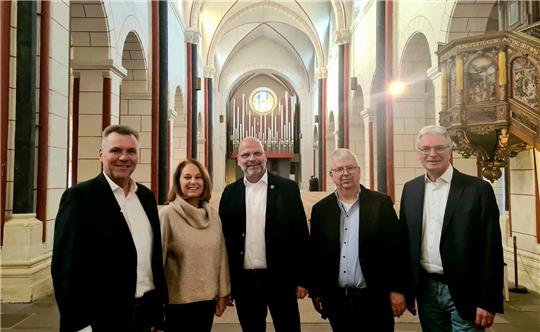 Vier Männer und eine Frau stehen im Kirchenschiff und lächeln in die Kamera. 