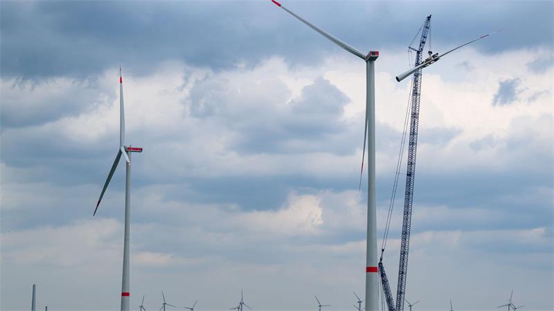 Lochtumer Bürgerinitiative gegen Windkraft informiert über Pläne Windkraftanlage mit drei Rotorblättern neben einem Kran unter bewölktem Himmel.
