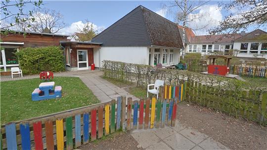 Außenbereich eines Kindergartens mit buntem Holzzaun, Spielgeräten und Gebäuden im Hintergrund