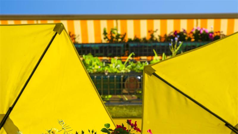 Balkon-Sommeridylle mit roten Blüten, gelben Schirmen und strahlendem Himmel