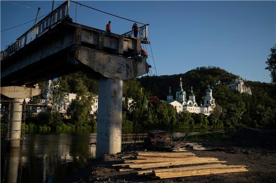 Bauarbeiter steigen von einer Leiter auf einer zerstörten Brücke neben dem Kloster Swjatohirsk herunter.