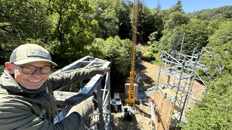 Bauherr Holger Kolb von Harz-Venture erklärt, wie die Wipfelerlebniswelt gebaut wird. Er steht hoch über den ersten Stahlmasten.