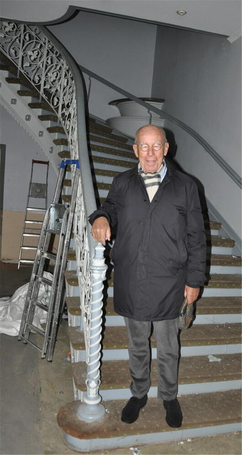 Zwei Goslarer Hotels mit Geschichte – und klaren Zukunftsplänen Mann in dunklem Mantel, grauer Hose und schwarzer Schuhen steht an einem Treppengeländer mit dekorativem Muster, im Hintergrund eine Leiter und eine gewundene Treppe.