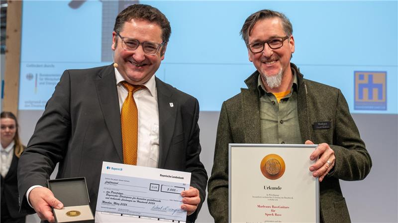 Bayerns Wirtschaftsstaatssekretär Tobias Gotthardt (l.) übergibt den Staatspreis an den Clausthaler Bassgitarrenhersteller Gerald Marleaux.