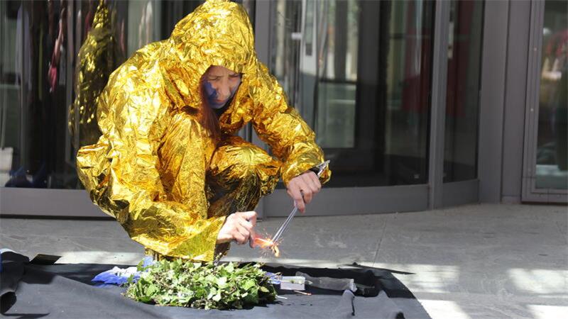 Person in goldfarbenem Rettungsfolie-Anzug hockt auf dem Boden und zündet ein Feuer an