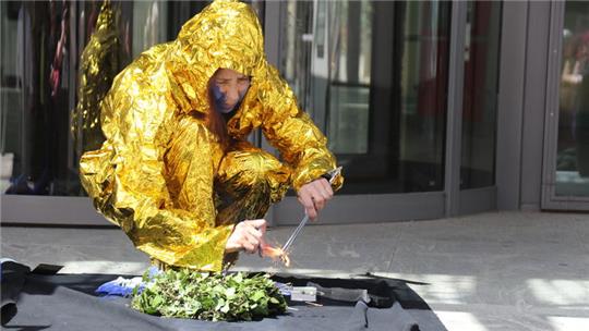 Person in goldfarbenem Rettungsfolie-Anzug hockt auf dem Boden und zündet ein Feuer an