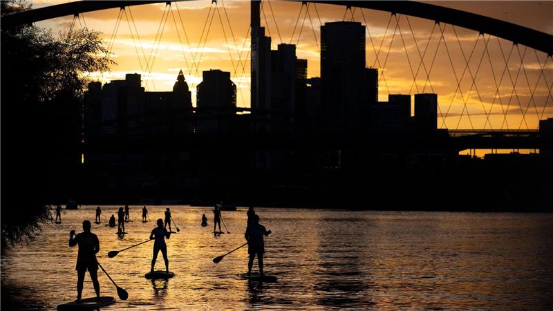 Bei Sicht auf die Skyline im letzten Licht des Tages fahren Stand-Up-Paddler in Nähe der Frankfurter Osthafenbrücke über den Main.