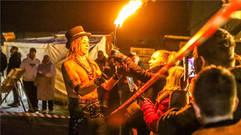 Eine Frau aus dem Publikum nimmt eine Fackel des Feuerkünstlers entgegen.