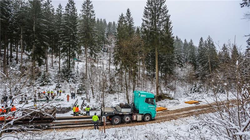 Das Bild zeigt ein Waldstück, in dem ein großer Lkw und mehrere Personen versammelt stehen.