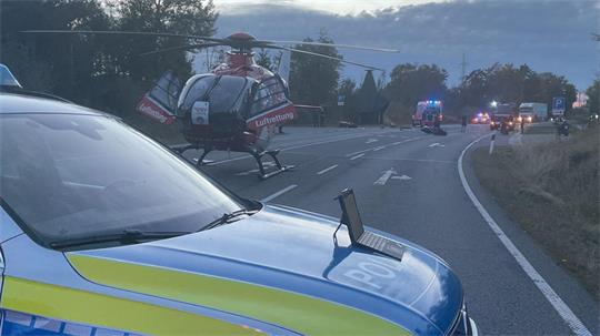 Polizeiauto mit Blaulicht auf einer Landstraße, im Hintergrund ein Rettungshubschrauber und weitere Einsatzfahrzeuge