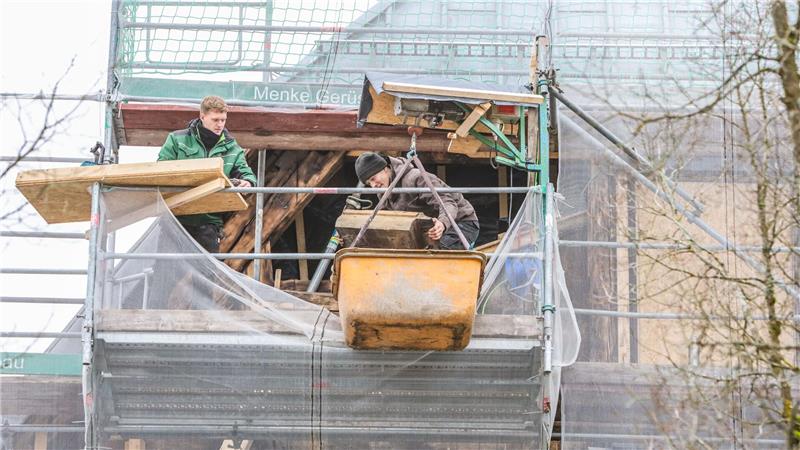 An der Marktkirche steht ein Gerüst, auf dem zwei Männer stehen. Sie legen die verkohlten Holzbalken frei und befördern sie mit einem Seilzug nach unten.