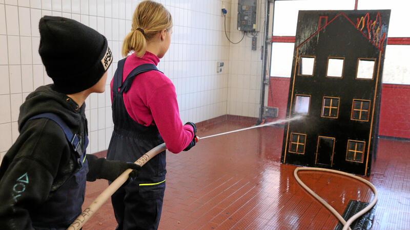 Kinder stehen mit dem Schlauch an der Spritzwand.