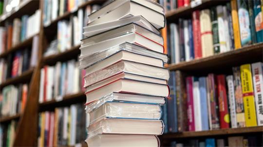 Das Foto zeigt einen Bücherstapel vor einem Bücherregal.