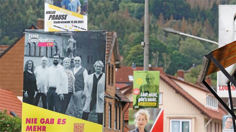 Plakat mit schwarz-weißer Gruppenaufnahme von fünf Personen vor Häusern und Wald im Hintergrund