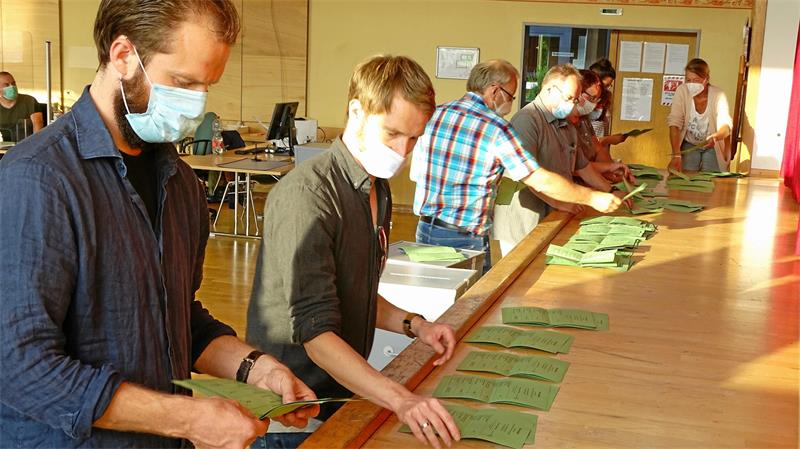 Menschen sortieren Wahlzettel auf mehrere Haufen. 