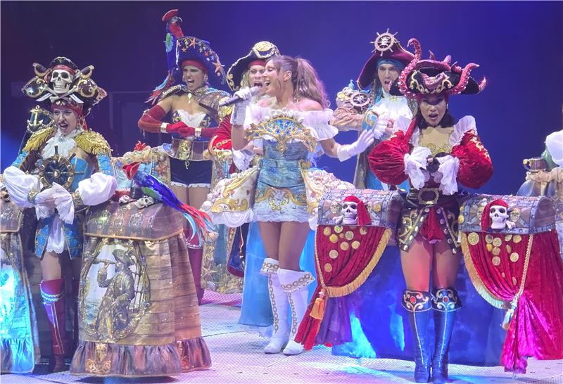 Osterfeld: Nach Neptuns Catwalk geht es zum Unterwasserball Gruppe von Personen in aufwendigen Piratenkostümen mit Schatztruhen und eine Sängerin in einem hellen, verzierten Kleid auf einer Bühne.