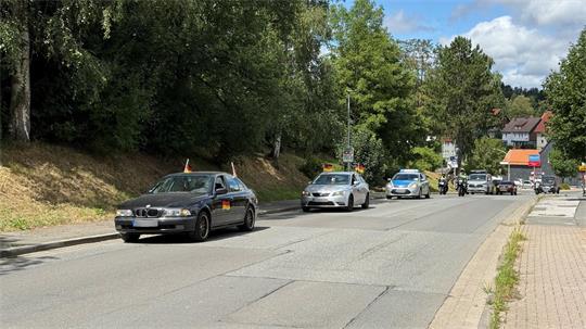 Mehrere Autos, die mit Deutschlandfahnen verziert sind, fahren mit Polizeibegleitung über eine Straße.