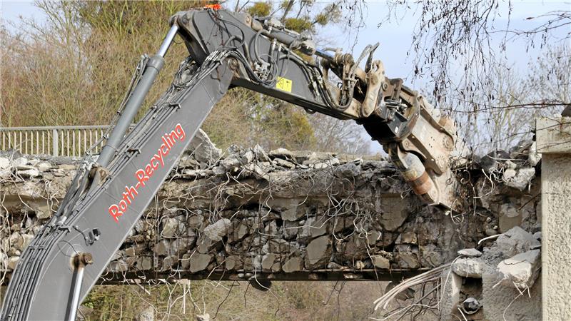 Ein Bagger knabbert mit einer Abbruchschere an einer Brücke.