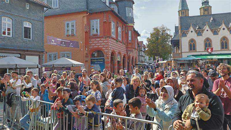 Mehrere Menschen stehen auf einem Marktplatz vor einer Absperrung.