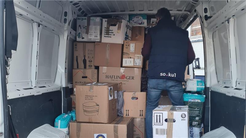 Person steht im Laderaum eines Lieferwagens vor einem Stapel aus Kartons und Paketen.