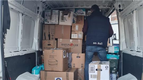 Person steht im Laderaum eines Lieferwagens vor einem Stapel aus Kartons und Paketen.