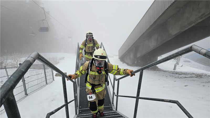 Feuerwehrleute laufen mit Ausrüstung eine steile Treppe hinauf. 