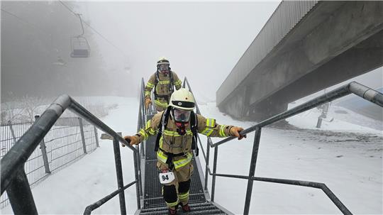 Feuerwehrleute laufen mit Ausrüstung eine steile Treppe hinauf. 