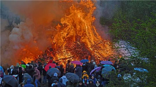 Große Menschenmenge mit Regenschirmen vor einem großen Osterfeuer in der Dämmerung.