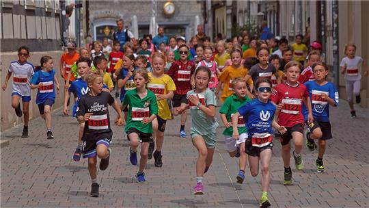 Gruppe von Kindern in Sportkleidung läuft auf gepflasterter Straße in einer Altstadt mit historischen Gebäuden im Hintergrund