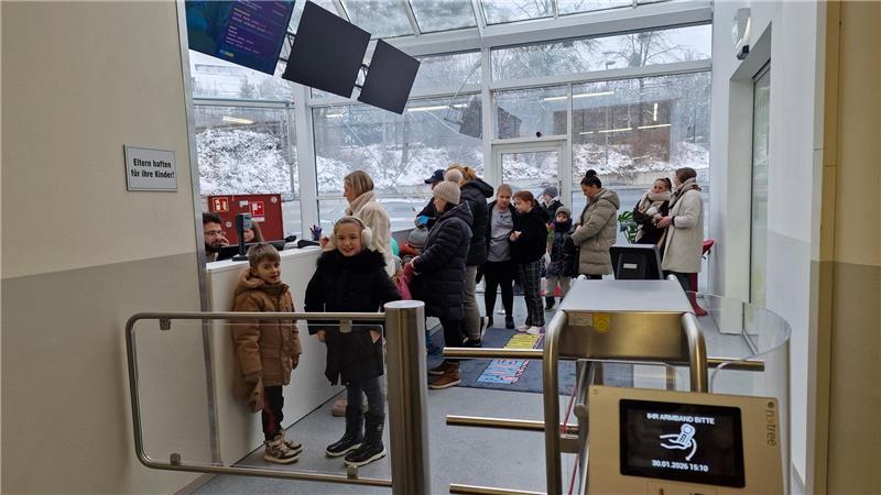 Menschen stehen in einer hellen Eingangshalle mit Glasdach und Schneelandschaft draußen in einer Warteschlange.