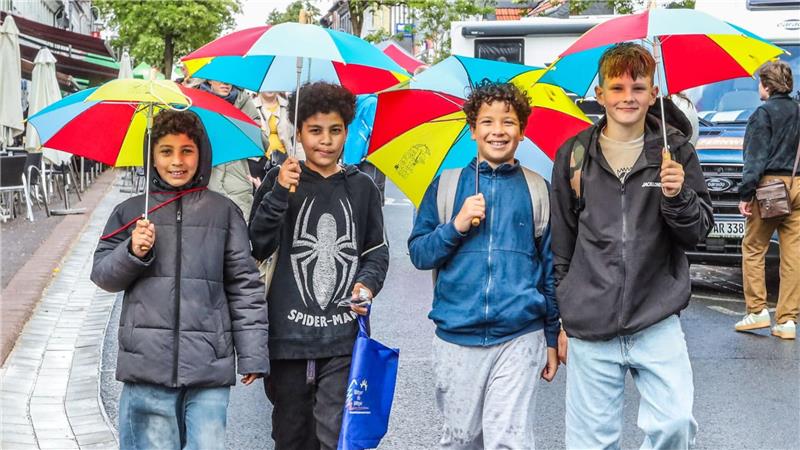 Vier Jungs laufen mit Regenbogen-Schirmen die Straße entlang.
