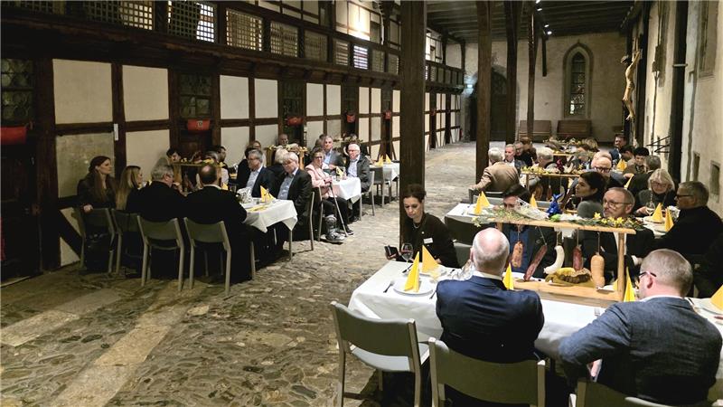 Großer Saal mit sichtbaren Holzbalken und mehreren Tischen, an denen Menschen sitzen und essen. 