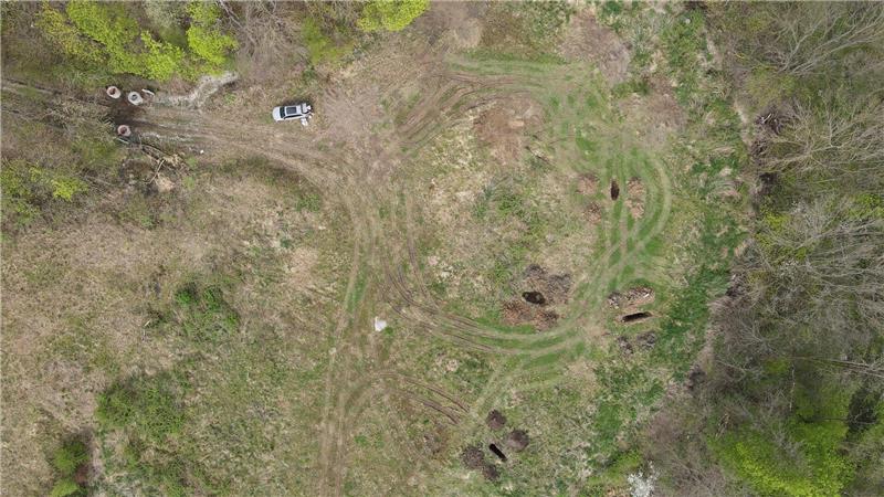 Luftaufnahme einer Wiese mit mehreren Erdhügeln, einem Auto und umgebenden Bäumen