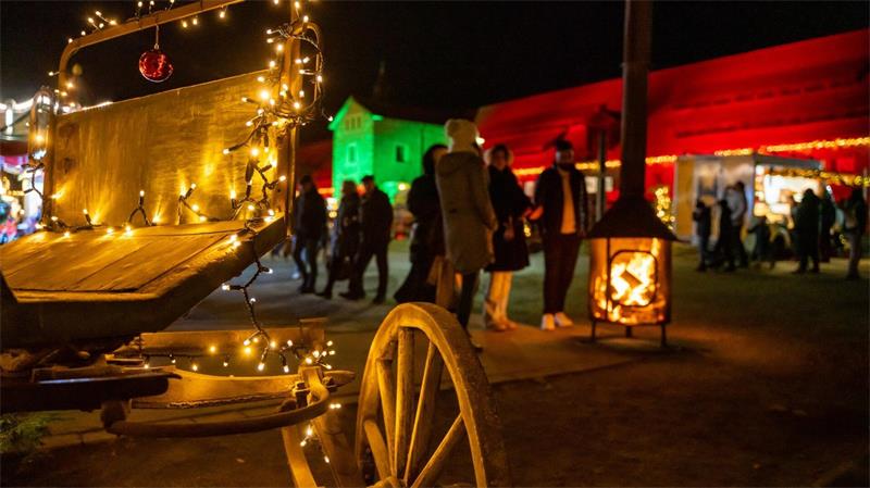 Eine mit einer Lichterkette geschmückte Kutsche, im Hintergrund ein grün und rot beleuchteter Stall.