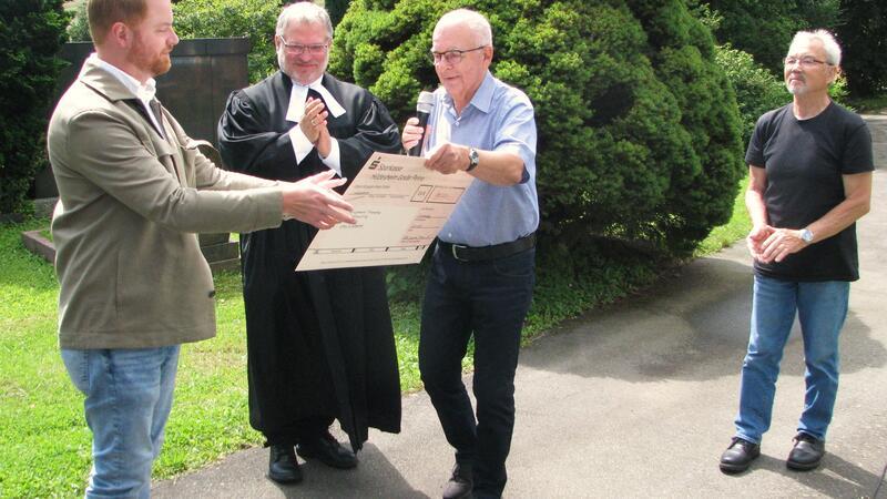 Bernd-Peter Rath, der Vorsitzende des Friedhof-Fördervereins, überreicht Frederik Kunze vom Kirchenvorstand und Pastor André Dittmann einen Scheck über 14.000 Euro für den Bergfriedhof in St. Andreasberg.