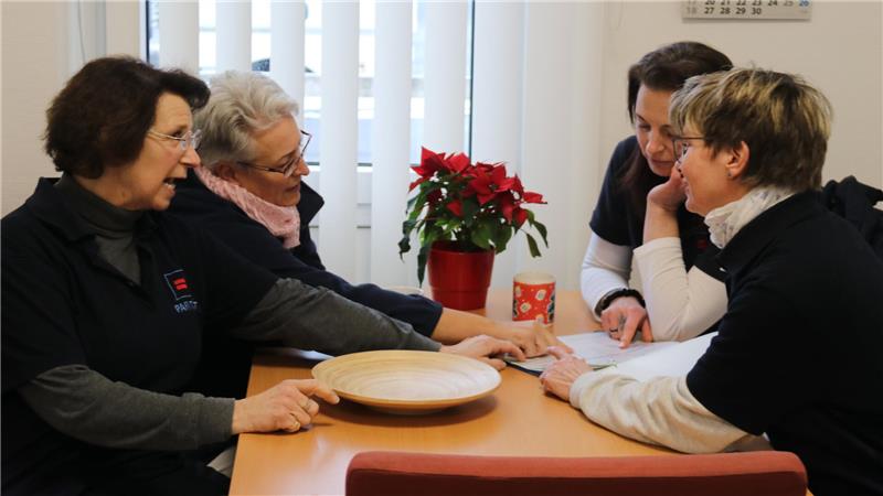 Vier Personen sitzen an einem Tisch mit einer Pflanze und einer Tasse darauf und diskutieren über Unterlagen.