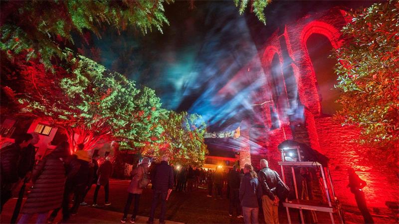 Besucher des Lichtkunstfestival Rheinleuchten wandeln durch den illuminierten Klostergarten in Oberwesel. 
