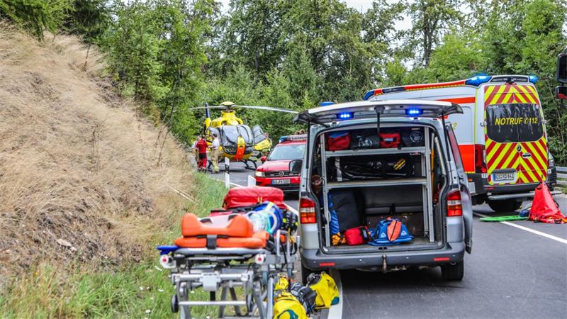 Rettungsfahrzeuge und ein Hubschrauber stehen auf einer Kurve auf einer Straße.